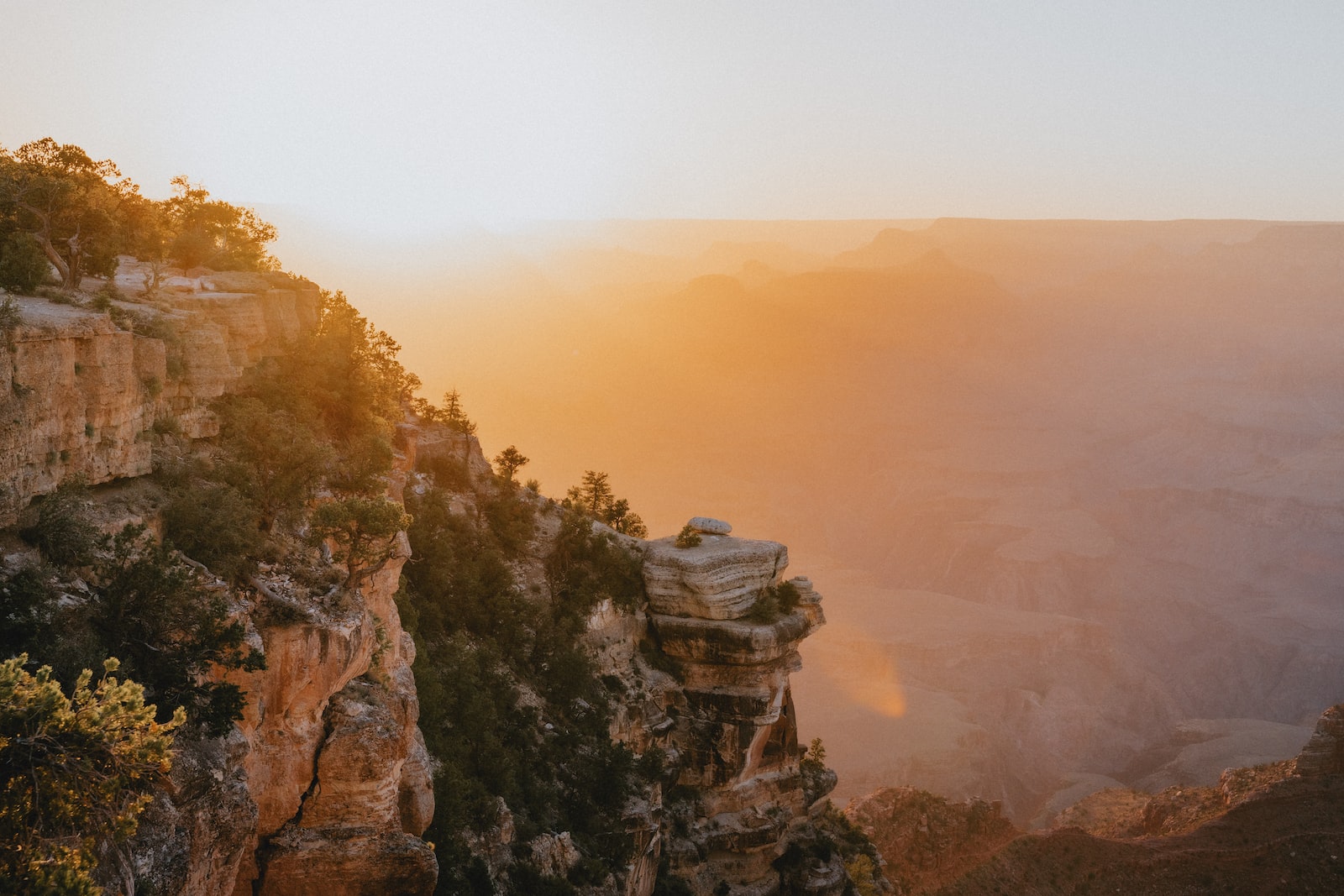 the sun is setting at the edge of a cliff